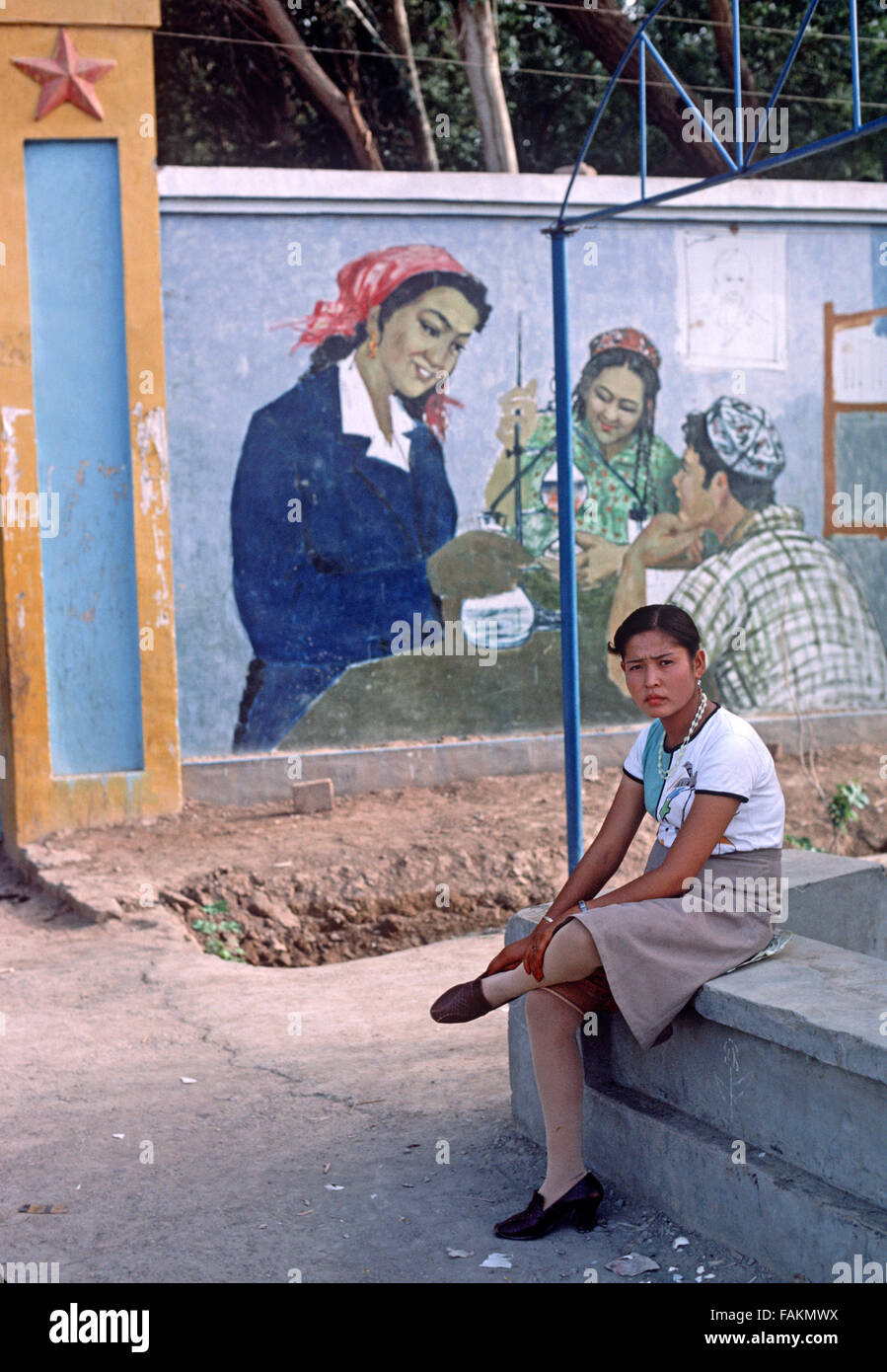 Uyghur Frau vor pädagogischen Wandbild, Turpan, Provinz Xinjiang, China Stockfoto
