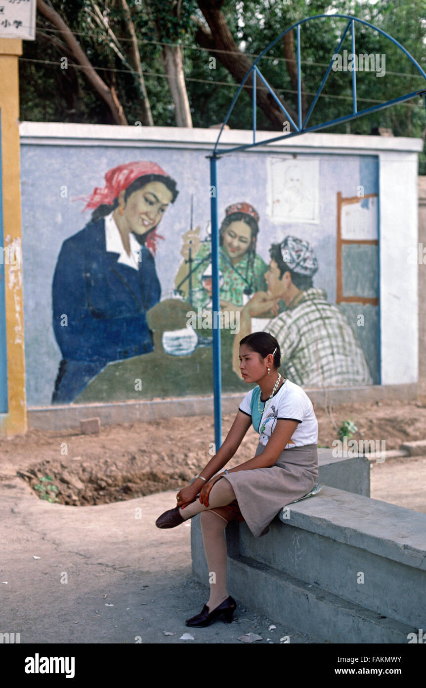 Uyghur Frau vor pädagogischen Wandbild, Turpan, Provinz Xinjiang, China Stockfoto