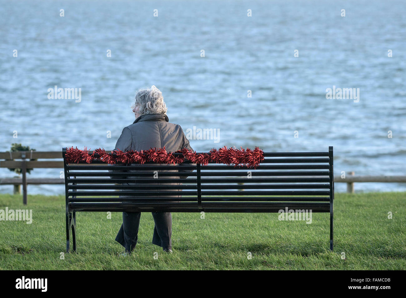 Eine Frau sitzt auf ihrem eigenen - eine einsame Frau sitzen auf einer Bank am East Beach in Shoeburyness in Essex, UK. Stockfoto