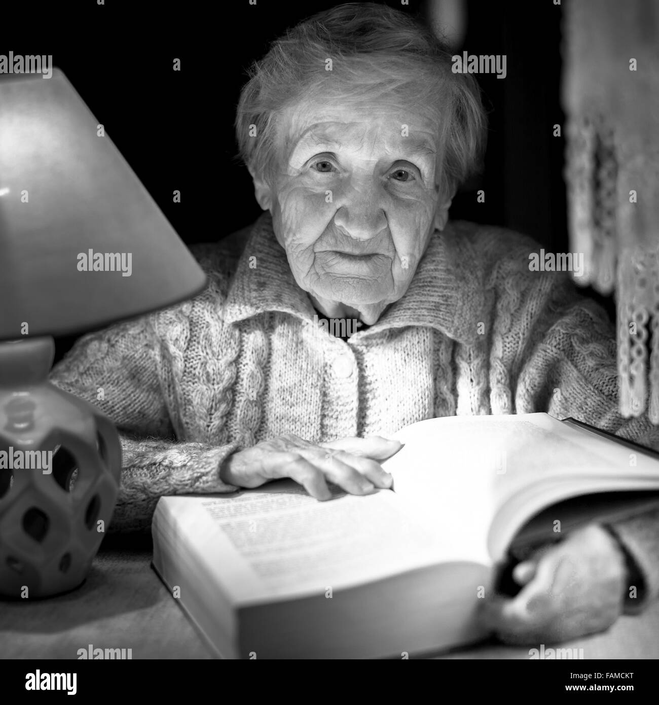 Eine alte Frau liest ein Buch, Nachtlicht, schwarz / weiß Fotografie. Stockfoto