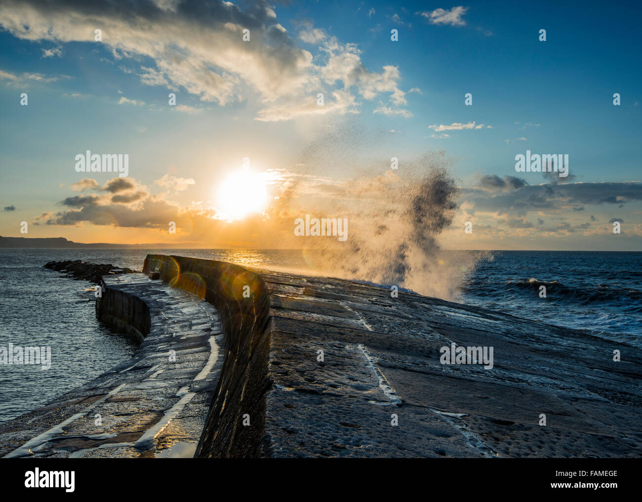 Sonnenaufgang über der Bucht von Lyme Regis, wie eine Welle bricht gegen den Cobb. Stockfoto