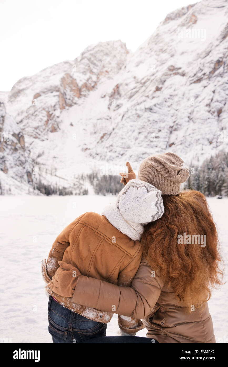 Winter Freizeit im Freien verbringen, zwischen schneebedeckten Gipfeln verwandeln den Urlaub in einer faszinierenden Reise. Gesehen von hinten weisenden Mutter Kind auf schneebedeckte Berge Stockfoto