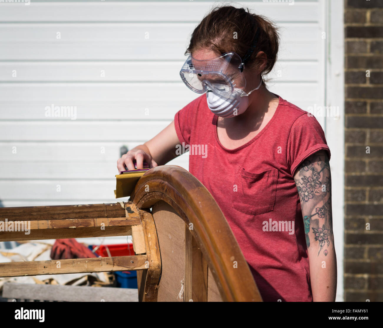 Tätowierte junge Frau Schleifen von hand ein Stück antike Holzmöbel außerhalb Ohrschutz. Stockfoto
