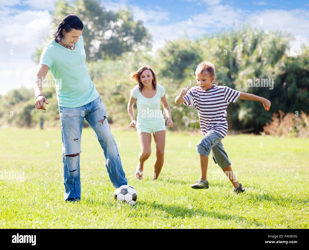 Glückliche Familie mit Teenager-Sohn spielen mit Fußball im Sommerpark Stockfoto