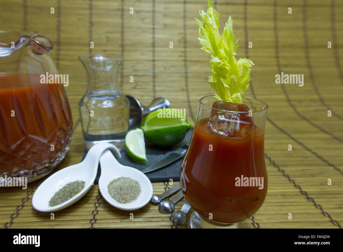 Glas mit Bloody Mary cocktail mit Sellerie und Eis Stiel auf Bambusmatte mit Tomatensaft und andere Befestigungen auf Eis. Stockfoto
