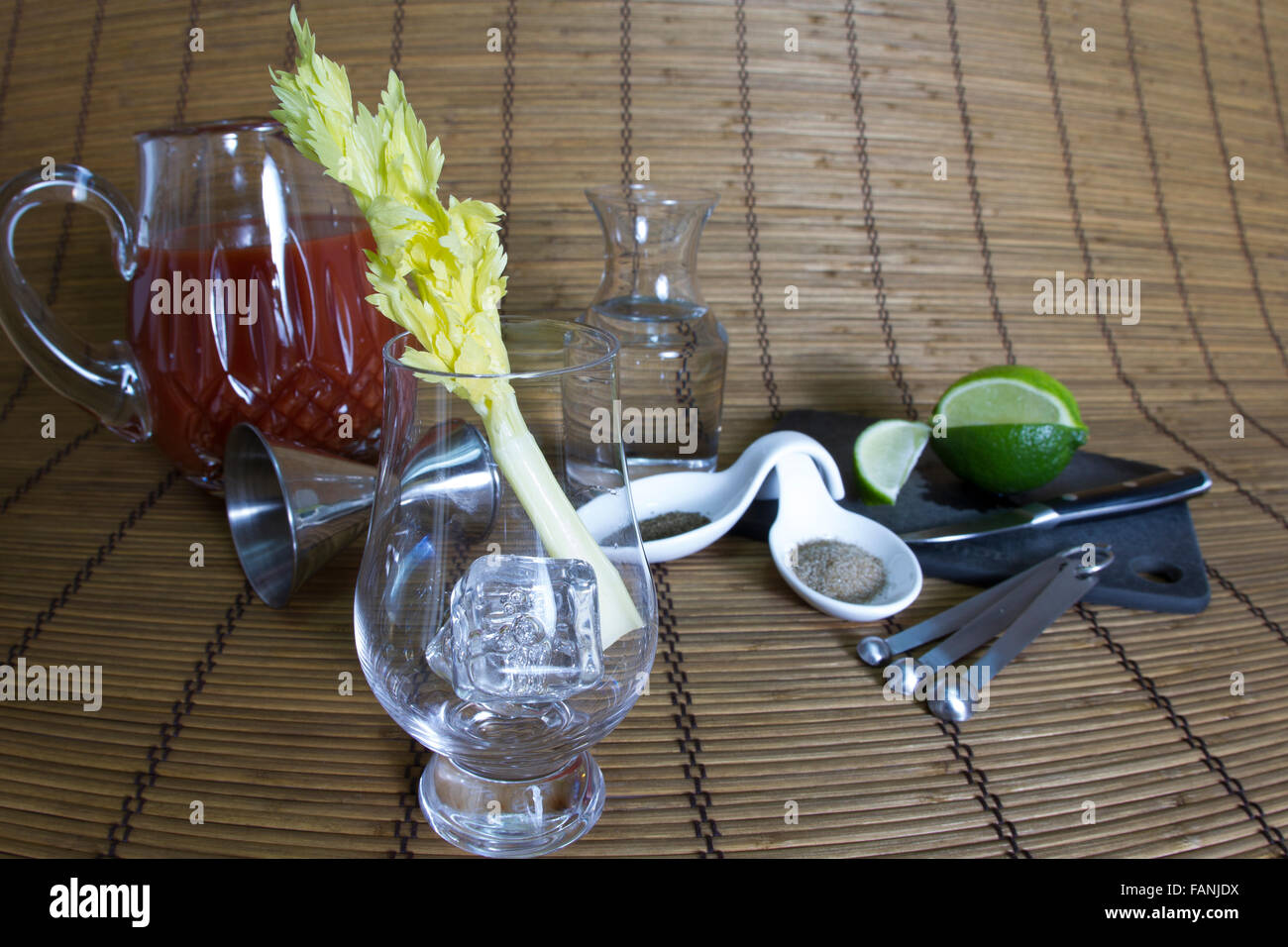 Leere Glas mit Eis und Sellerie Stengel auf Bambusmatte mit Tomatensaft und andere Befestigungen für Bloody Mary cocktail. Stockfoto