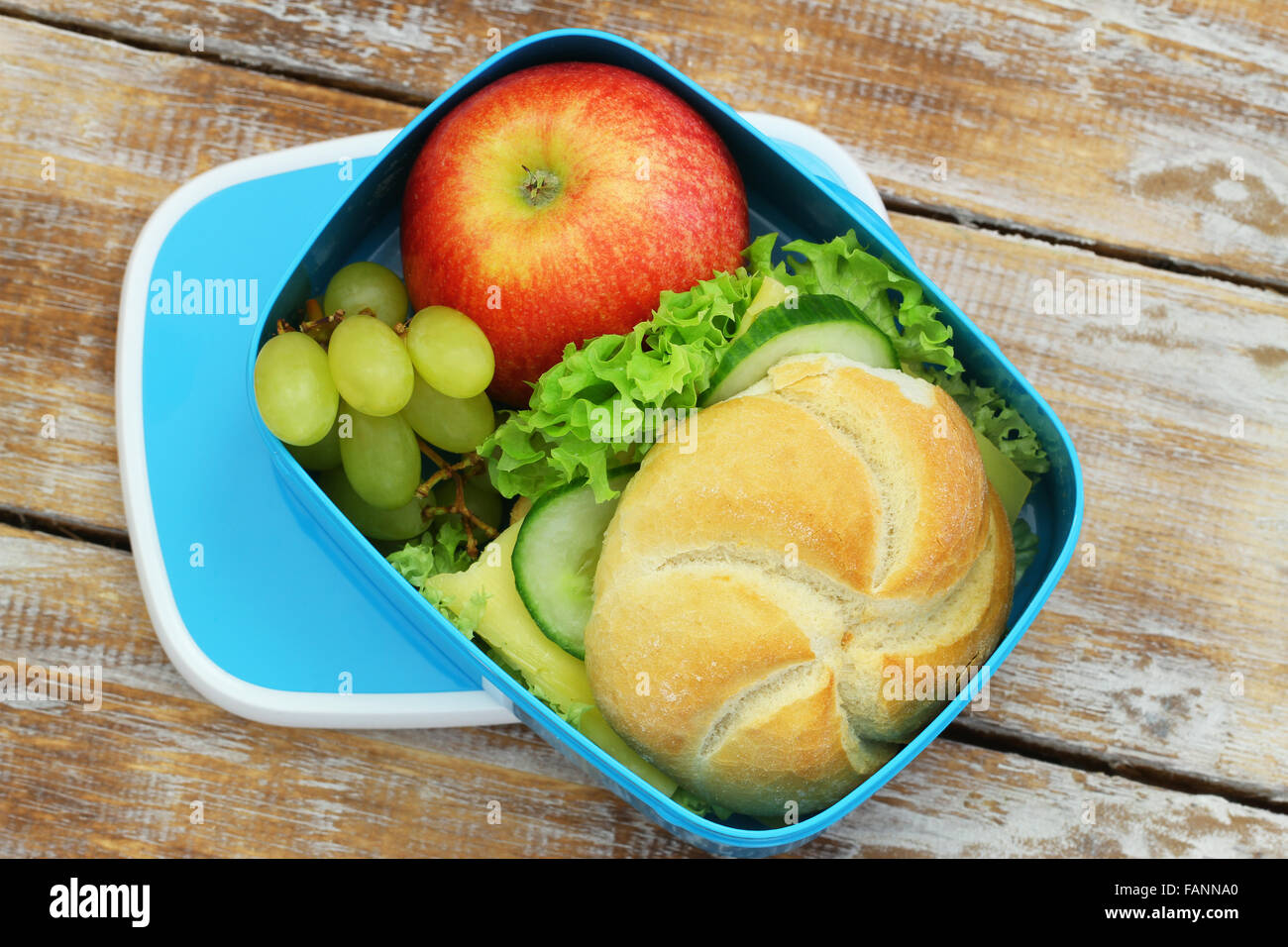 Lunch-Box mit Brötchen mit Käse und Salat, Trauben und roter Apfel Stockfoto