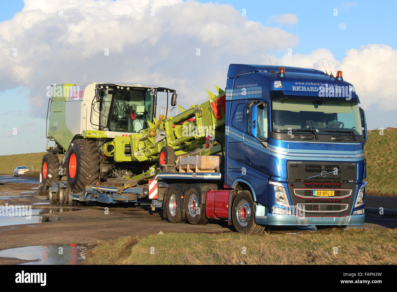 EIN BLAUER VOLVO-LKW AUS DEN NIEDERLANDEN LIEFERT EINE NEUE GRÜNE MÄHDRESCHER ZU EINEM UK-BAUERNHOF Stockfoto