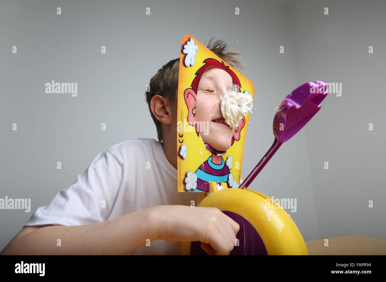 Ein Junge spielt das Brettspiel Pie Gesicht von Hasbro in Creme bedeckt Stockfoto