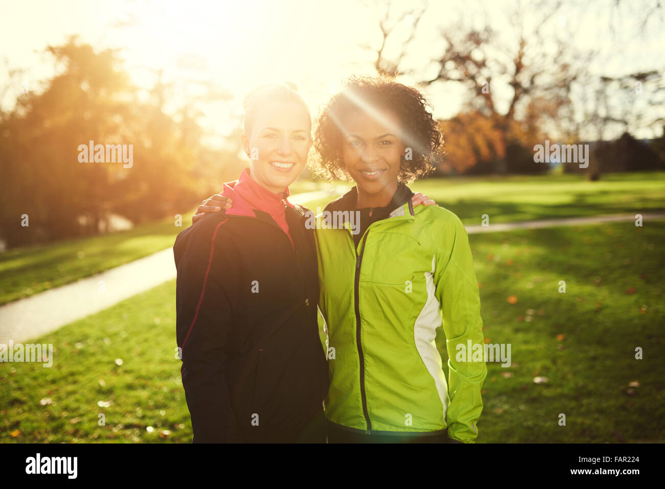 Zwei junge Sportlerinnen umarmt und lächelt in die Kamera, während Sie im Park stehen. Sonnig Stockfoto