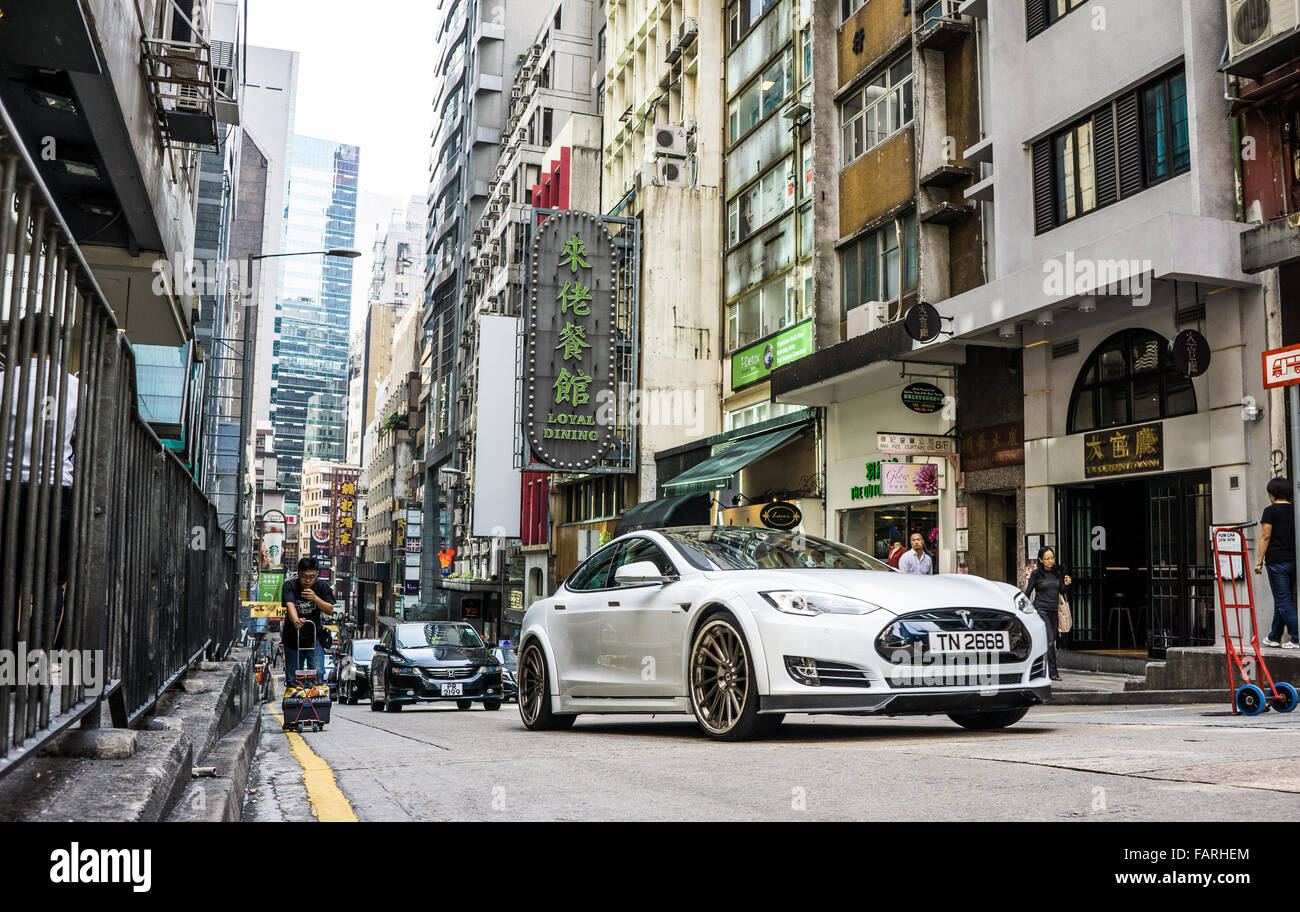 Ein beschäftigt Hong Kong Straßenszene mit einem Tesla-Auto im Vordergrund Stockfoto
