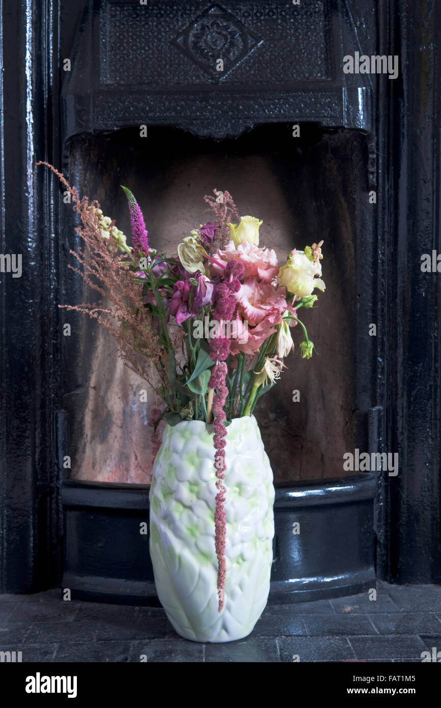 Eine Vase mit Blumen vor einem schwarzen Gusseisen Kamin sitzen Stockfoto