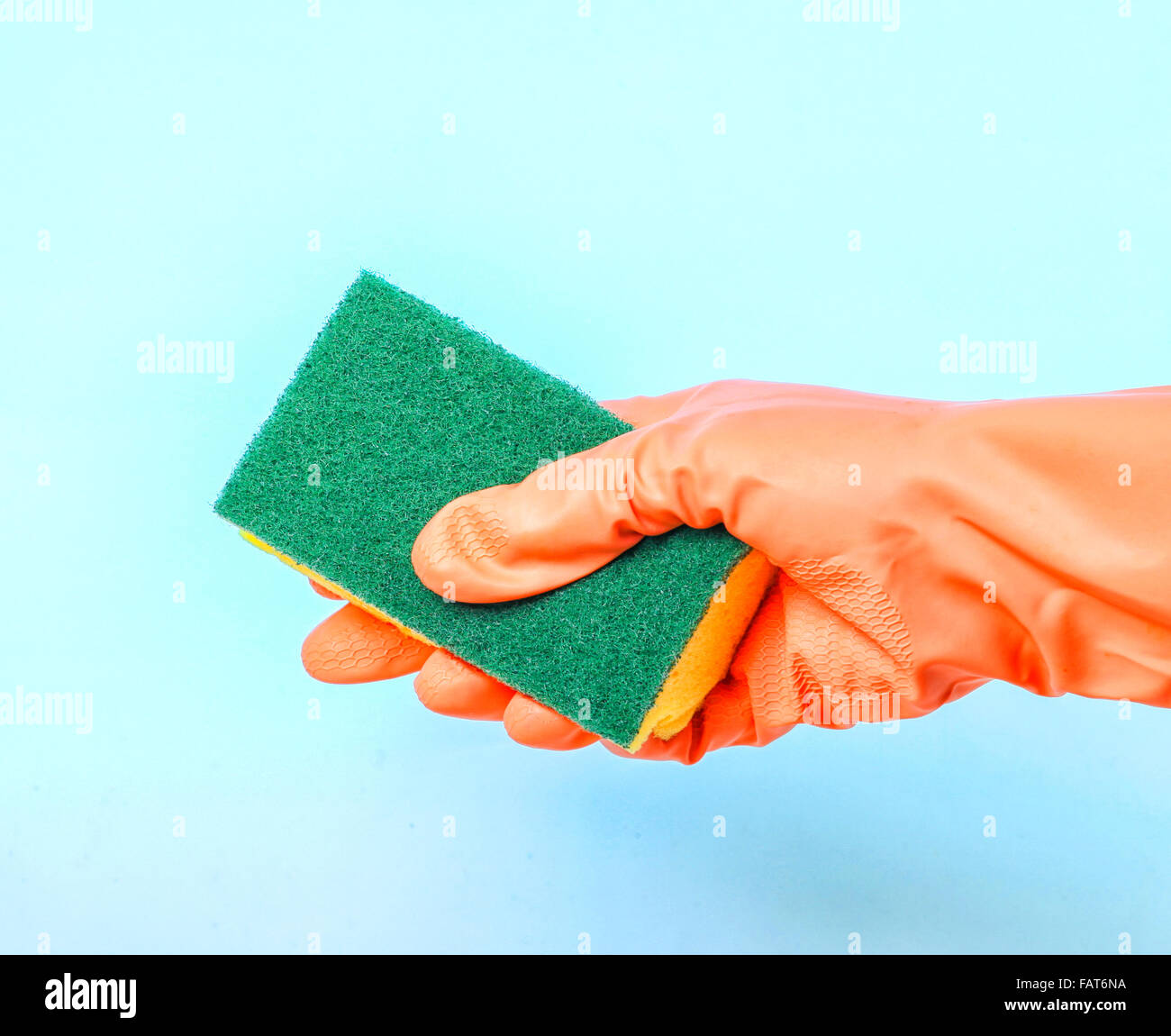 Hand mit orange Handschuh hält Reinigungsschwamm auf blauem Hintergrund Stockfoto