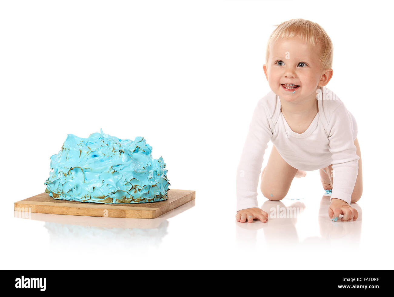 Ein einjähriges Baby junge Zerschlagung einer blauen Geeiste Geburtstagstorte auf einem Holzbrett. Bild wird auf einem weißen Hintergrund isoliert. Stockfoto