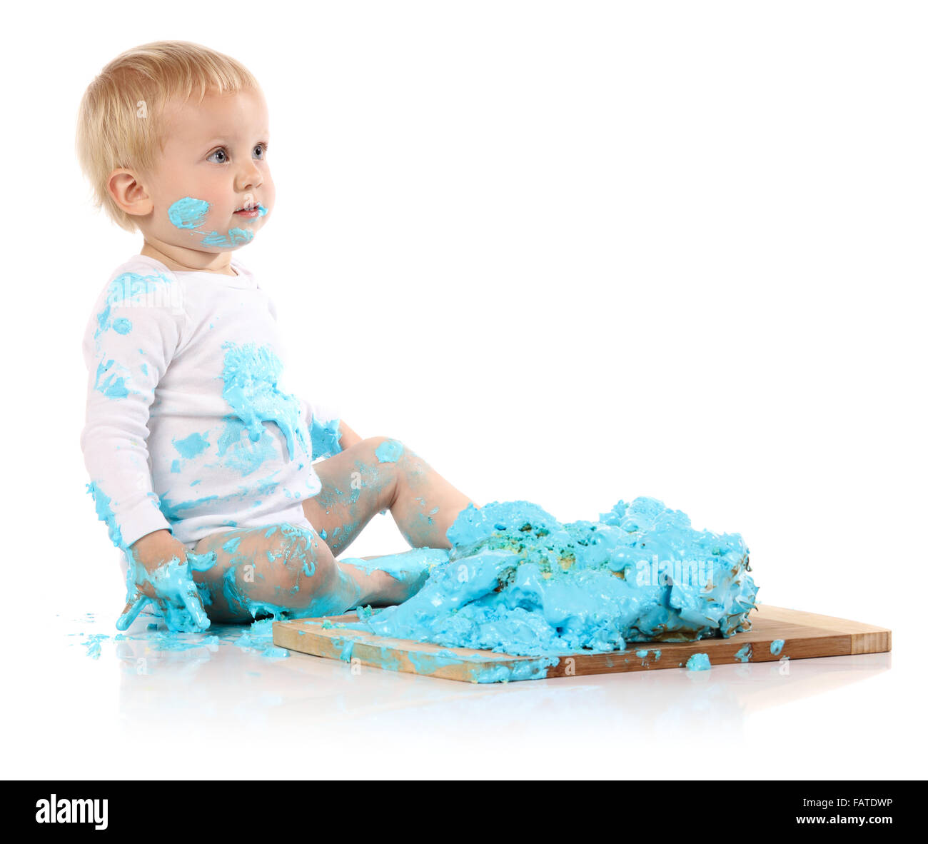 Ein einjähriges Baby junge Zerschlagung einer blauen Geeiste Geburtstagstorte auf einem Holzbrett. Bild wird auf einem weißen Hintergrund isoliert. Stockfoto