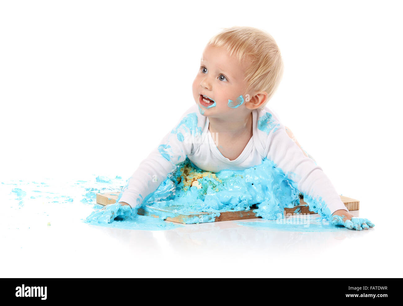 Ein einjähriges Baby junge Zerschlagung einer blauen Geeiste Geburtstagstorte auf einem Holzbrett. Bild wird auf einem weißen Hintergrund isoliert. Stockfoto