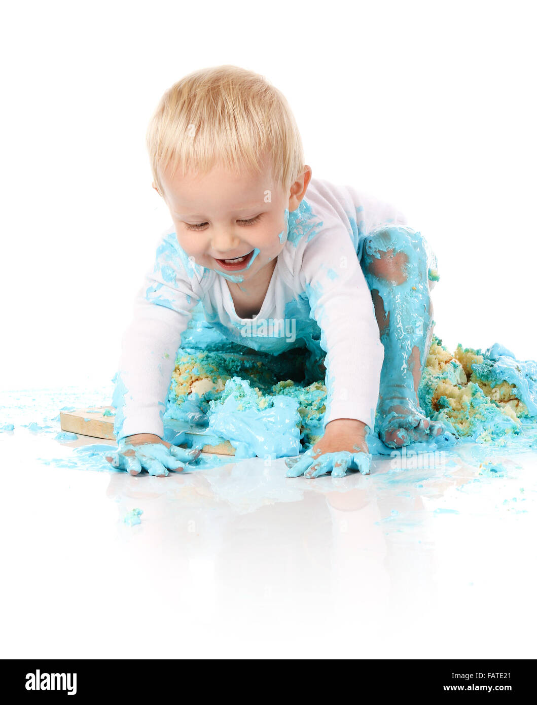 Ein einjähriges Baby junge Zerschlagung einer blauen Geeiste Geburtstagstorte auf einem Holzbrett. Bild wird auf einem weißen Hintergrund isoliert. Stockfoto