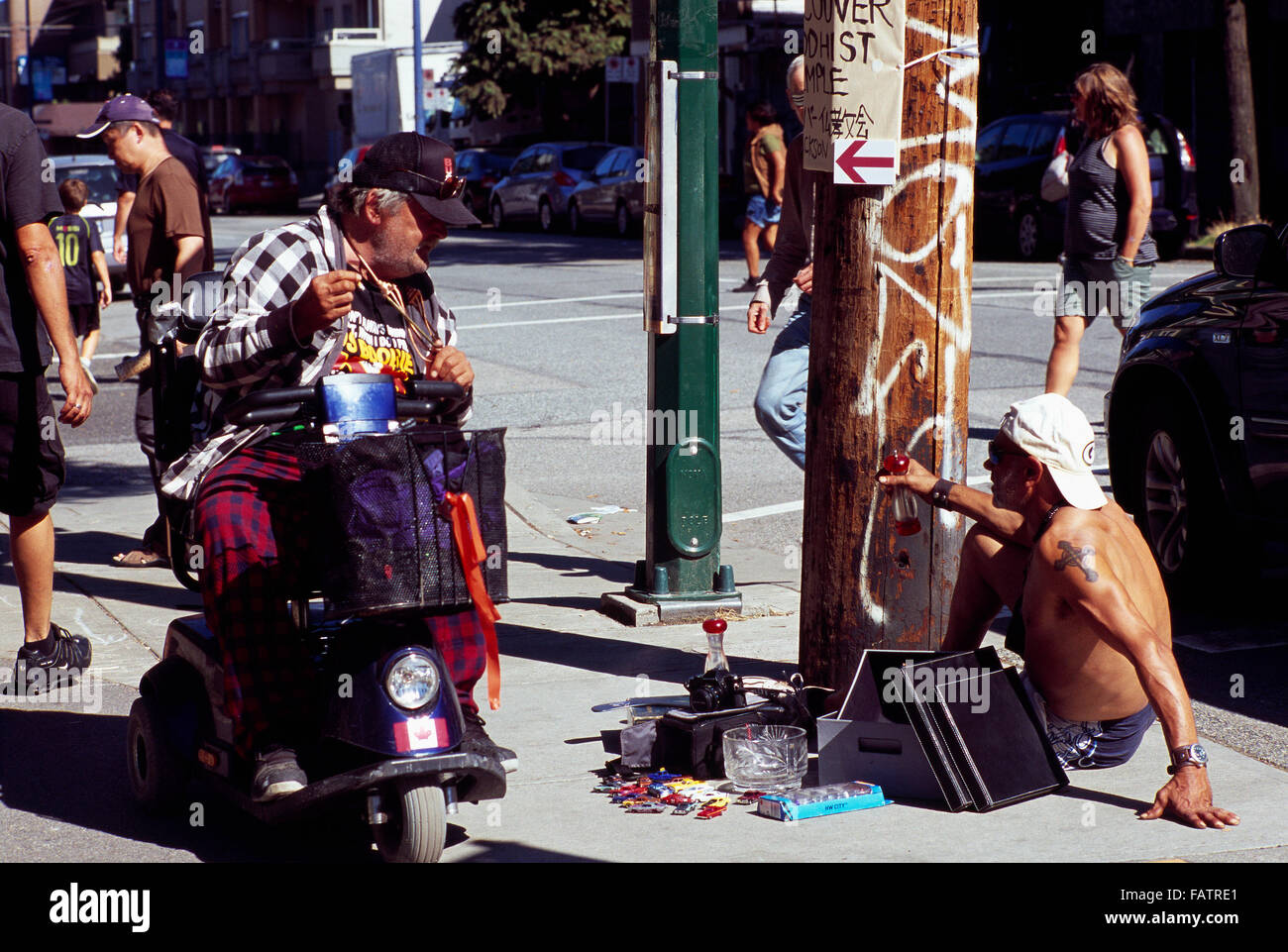 Downtown Eastside Vancouver, British Columbia, Kanada - Street Life Mann auf Mobilität Roller Gespräch mit Mann auf Gehweg zu verkaufen Stockfoto