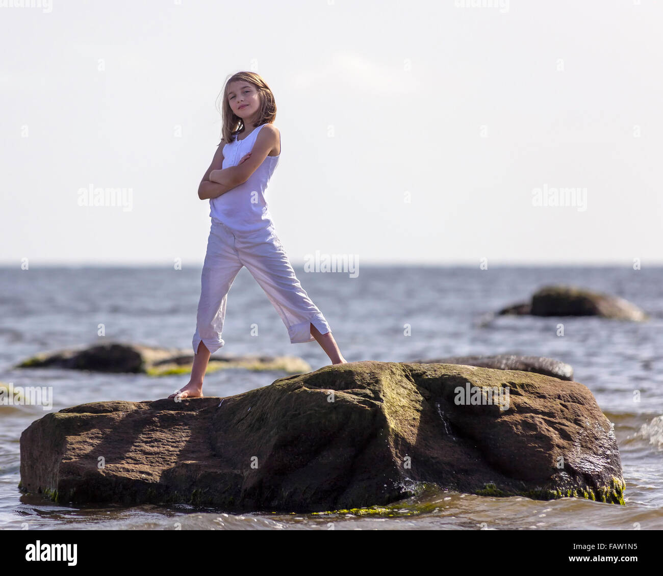 Junges Mädchen steht auf einem Felsen im Meer Selbstsicher und stark Model Release: Ja. Property Release: Nein. Stockfoto