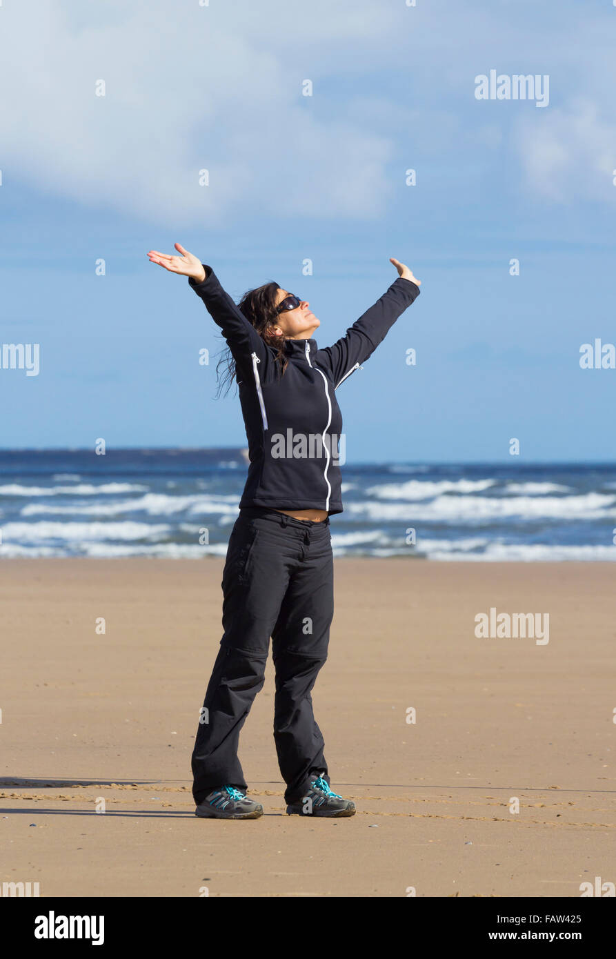 Weibliche Jogger lächelnd mit ausgestreckten am Strand an einem sonnigen Tag. Stockfoto