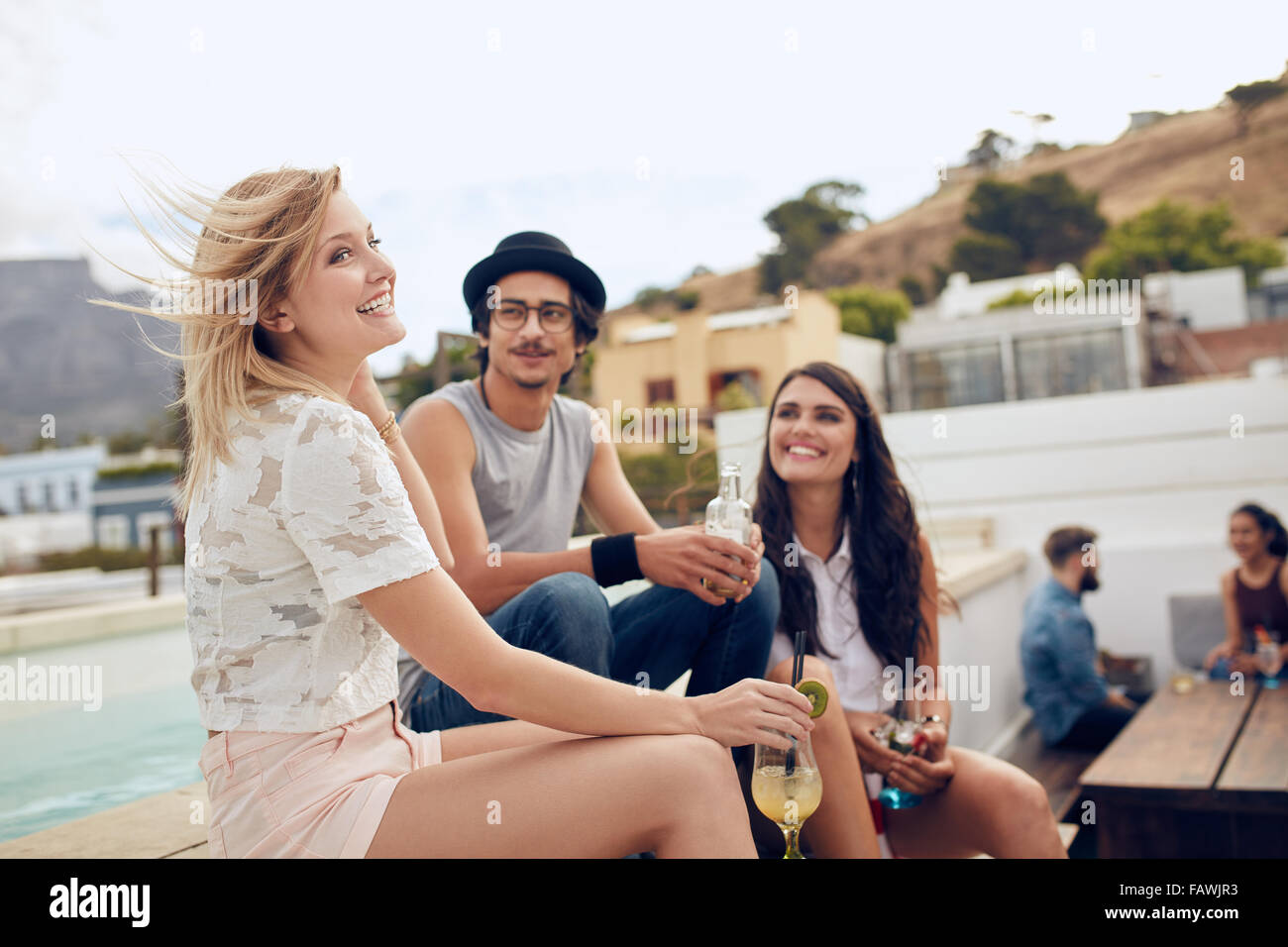 Gruppe junger Leute sitzen im Freien mit Getränke. Multirassische junge Freunde während einer Party auf der Dachterrasse genießen. Stockfoto