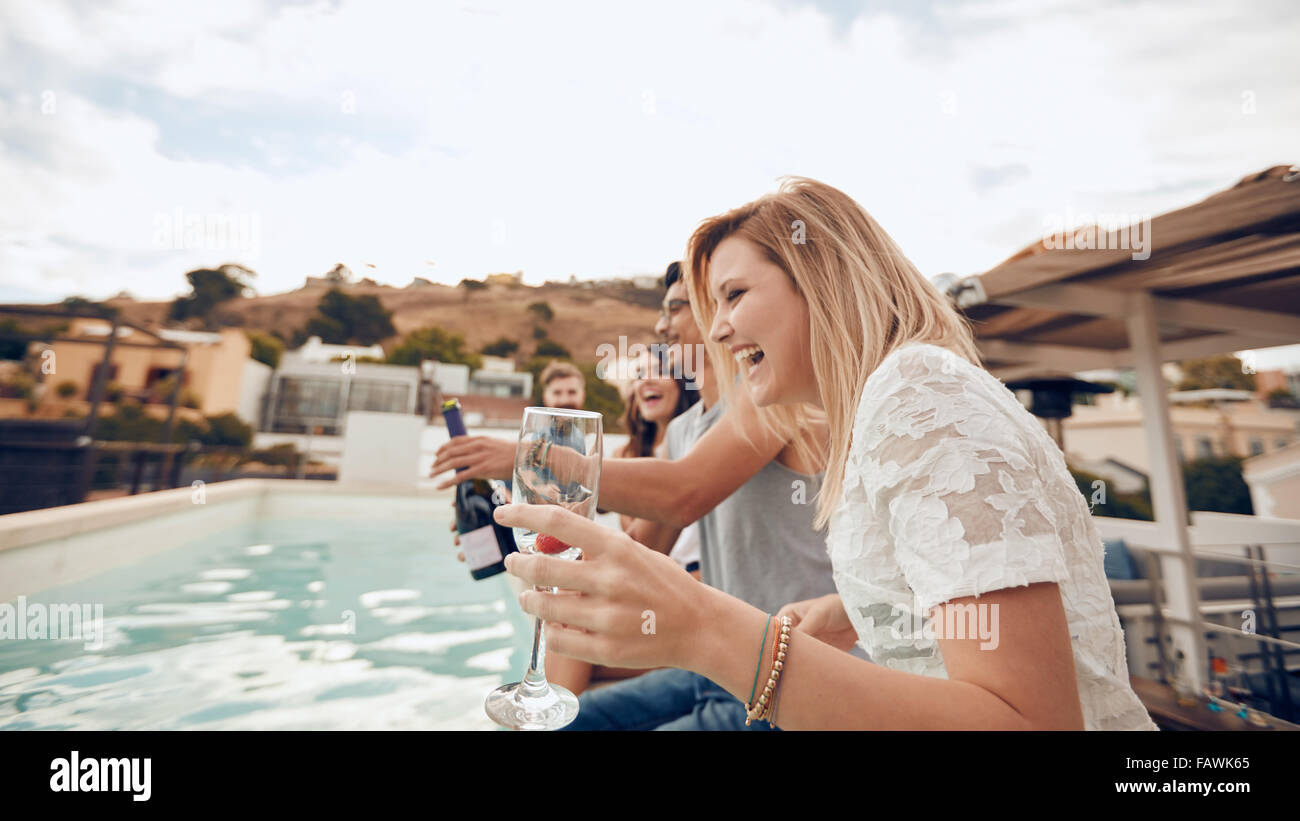 Jugendliche trinken am Pool während der Partei. Junge Freunde lachen während der Sitzung von einem Schwimmbad. Männer und Frauen feiern Stockfoto
