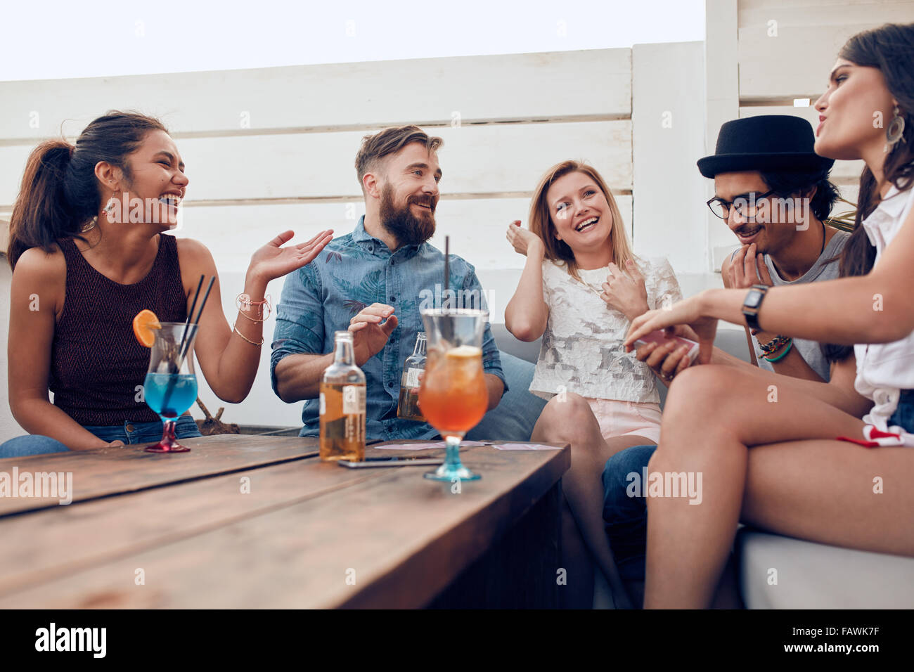 Porträt der glückliche junge Menschen zusammensitzen und lachen. Gemischtrassig Freunde auf einer Party mit Cocktails am Tisch genießen. Stockfoto