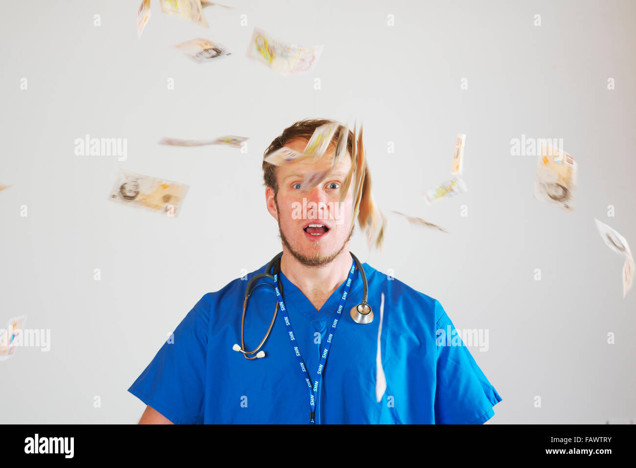 Junge weiße männliche Junioren Krankenhausarzt im Theater Blues tragen ein Stethoskop wirft eine Handvoll von zehn Pfund-Noten in die Luft Stockfoto