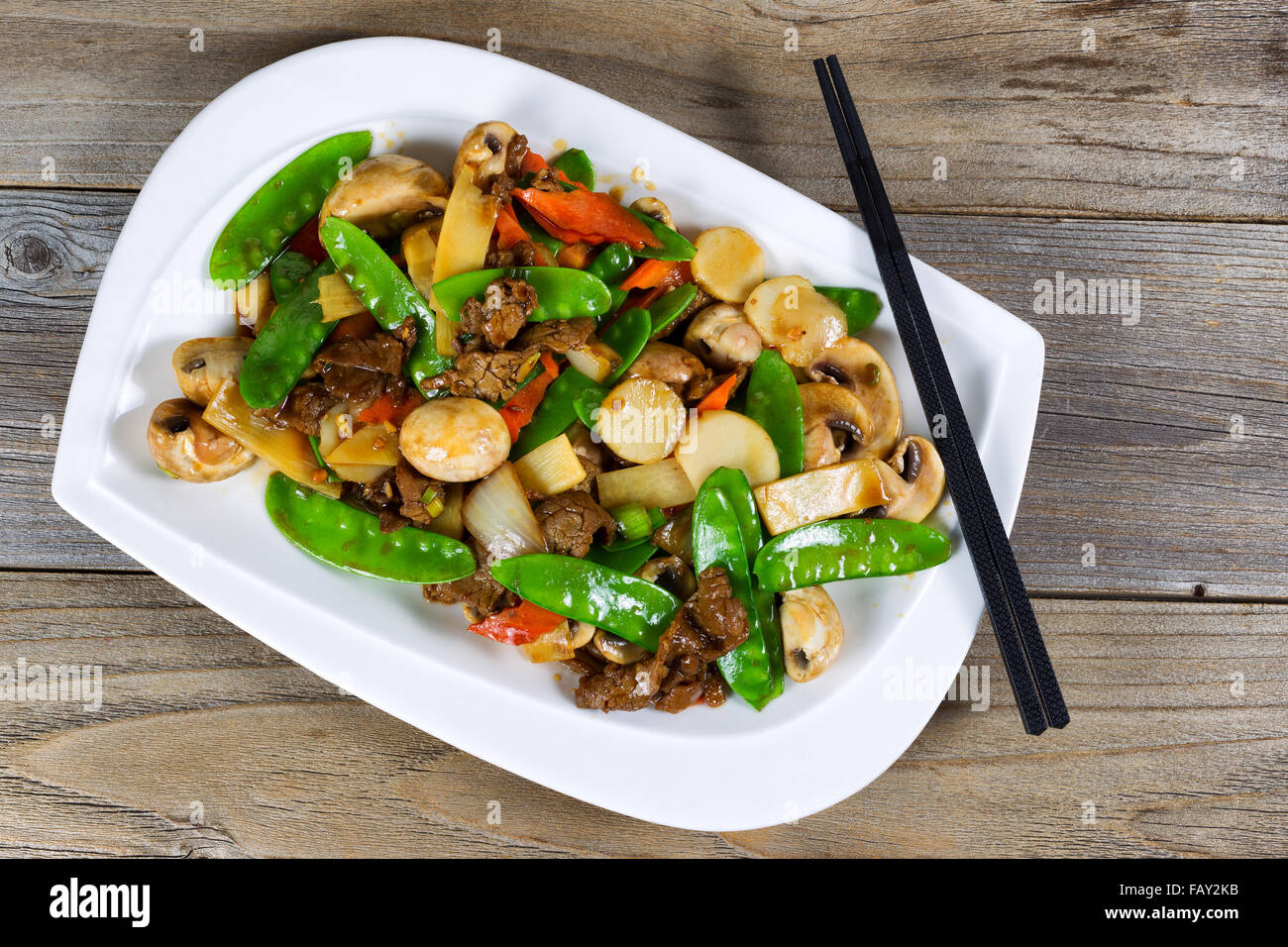 Hoher seitlicher Blick auf asiatischen Gericht bestehend aus geschnittenen saftiges Rindfleisch Reis, Zwiebel, Pilze, grüne Erbsen und Paprika. Stäbchen auf Stockfoto
