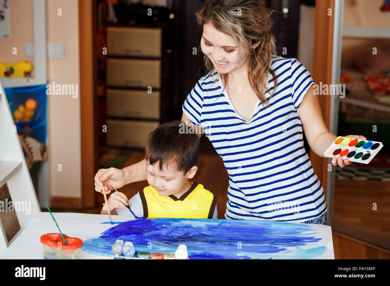 Fröhliche Kindheit, kleiner Junge spielt mit seiner Mutter, zeichnet, malt auf den Handflächen. Unterricht für Kinder zeichnen, Entwicklung von kreativen Fähigkeiten. Zeichnen Sie ein Meer. Stockfoto