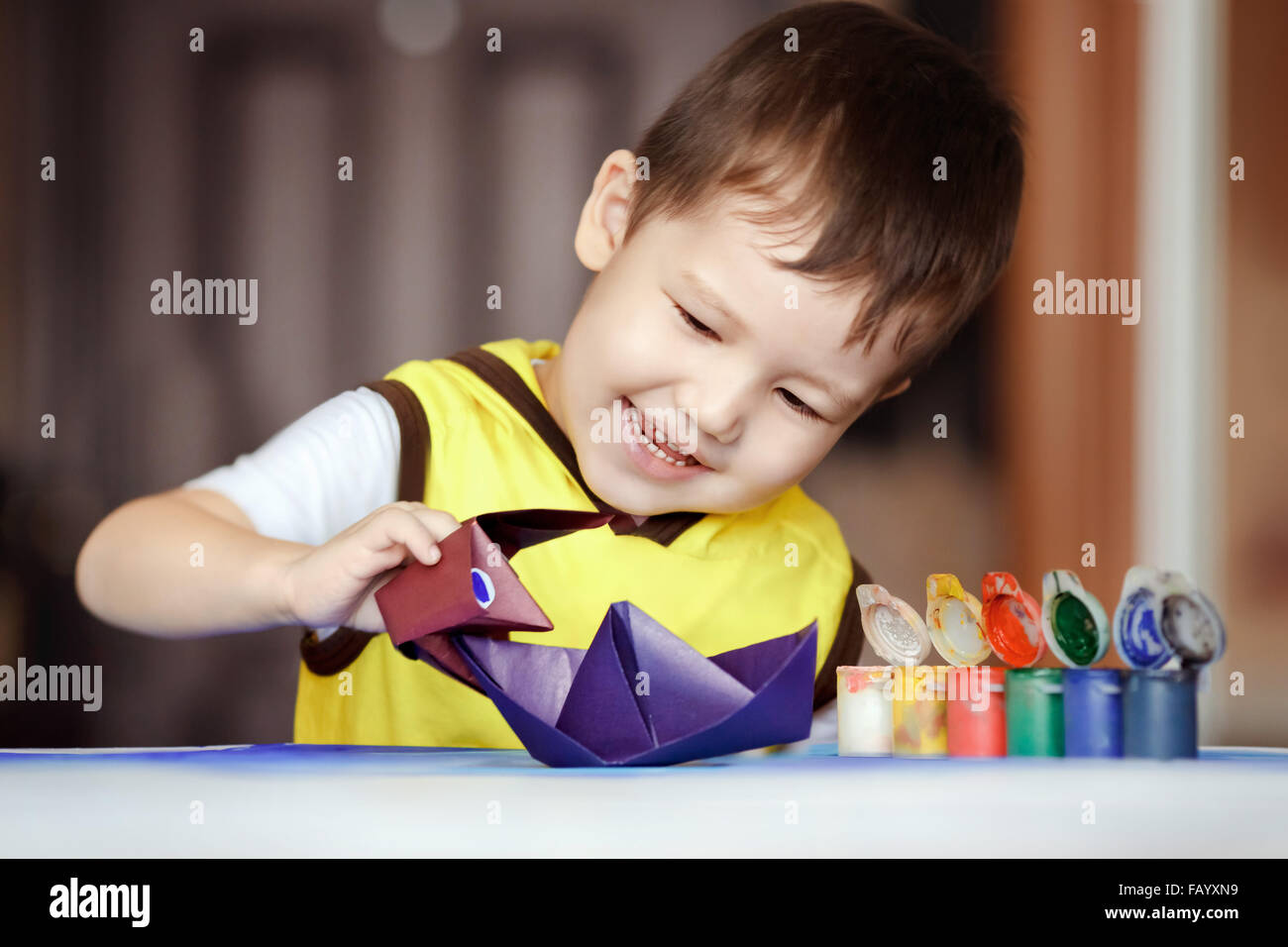 Kind spielt Seeschlacht, eine Origami-Figur Godzilla greift eine Boot, Spiele für Kinder. Die Entwicklung der Vorstellungskraft und des kreativen Denkens, Kunst Papierspielzeug zu schaffen. Violette Schiff. Stockfoto