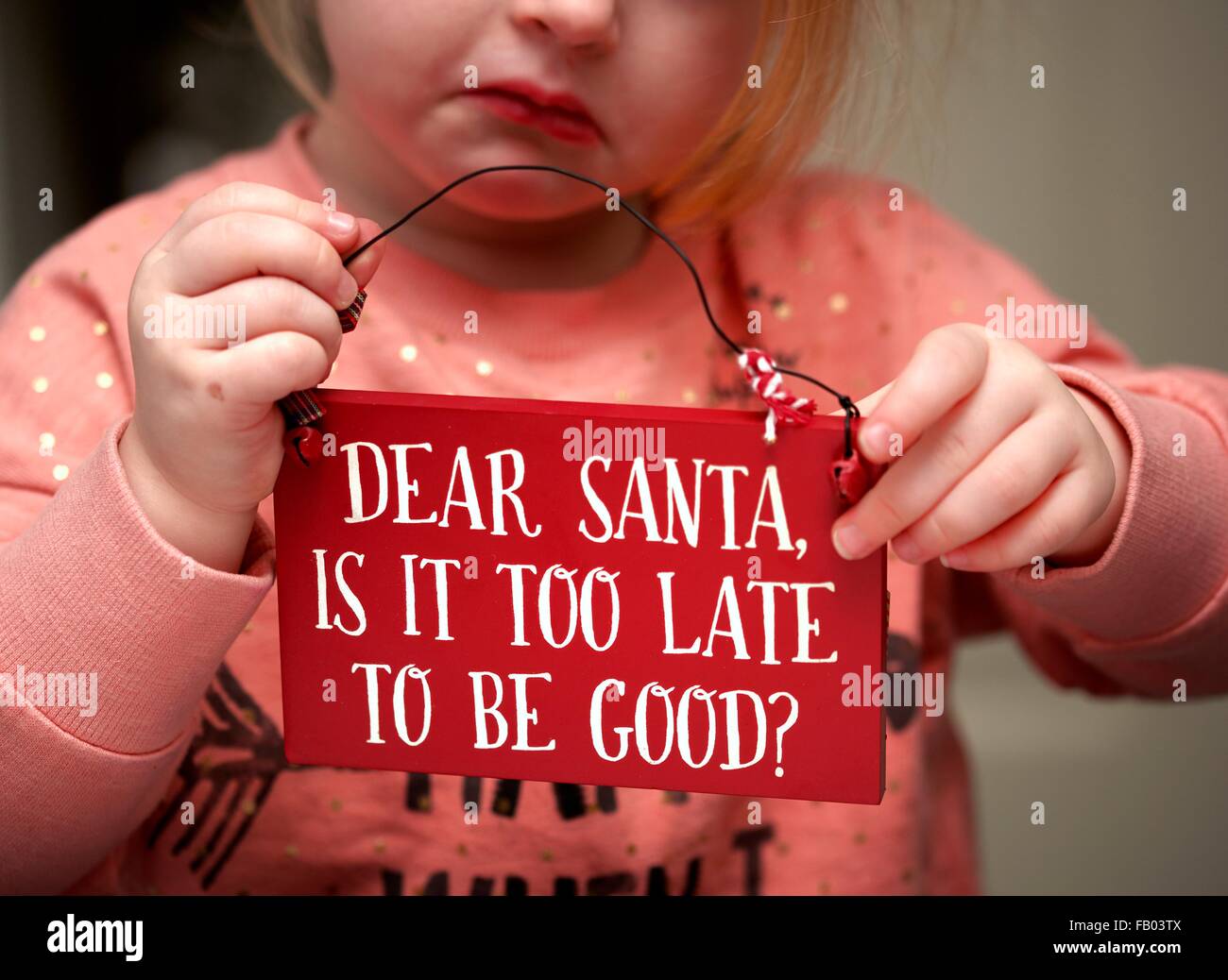 Ein 3-jähriges Mädchen mit einem traurigen Gesicht hält eine Plakette mit der Nachricht lieber Weihnachtsmann ist es zu spät, gut zu sein? Stockfoto
