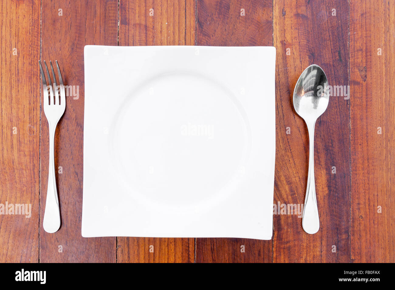 weißen Teller, Löffel und Gabel auf einem braunen Holztisch. Stockfoto