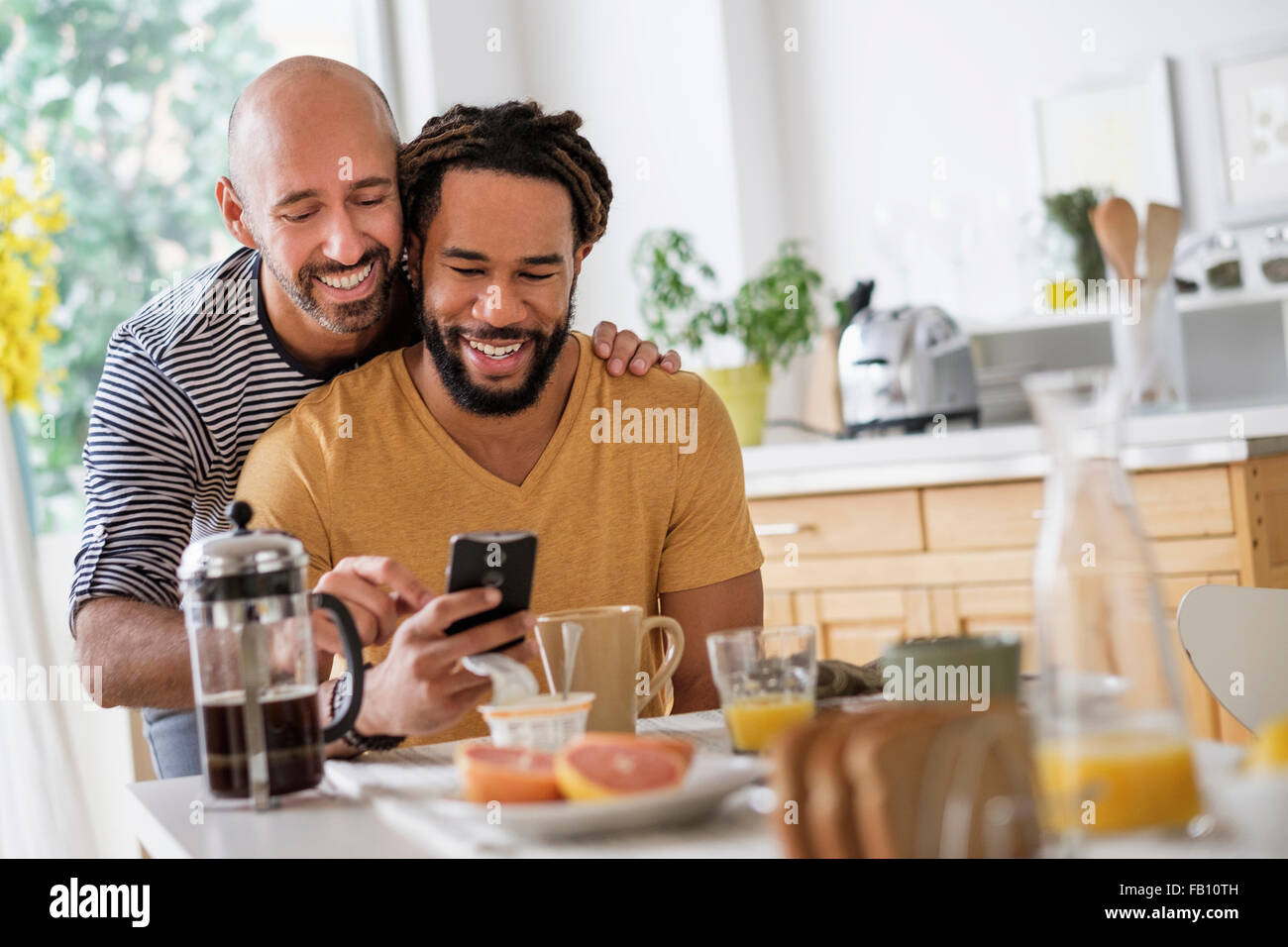 Smiley homosexuelle Paare mit Smartphone am Esstisch Stockfoto