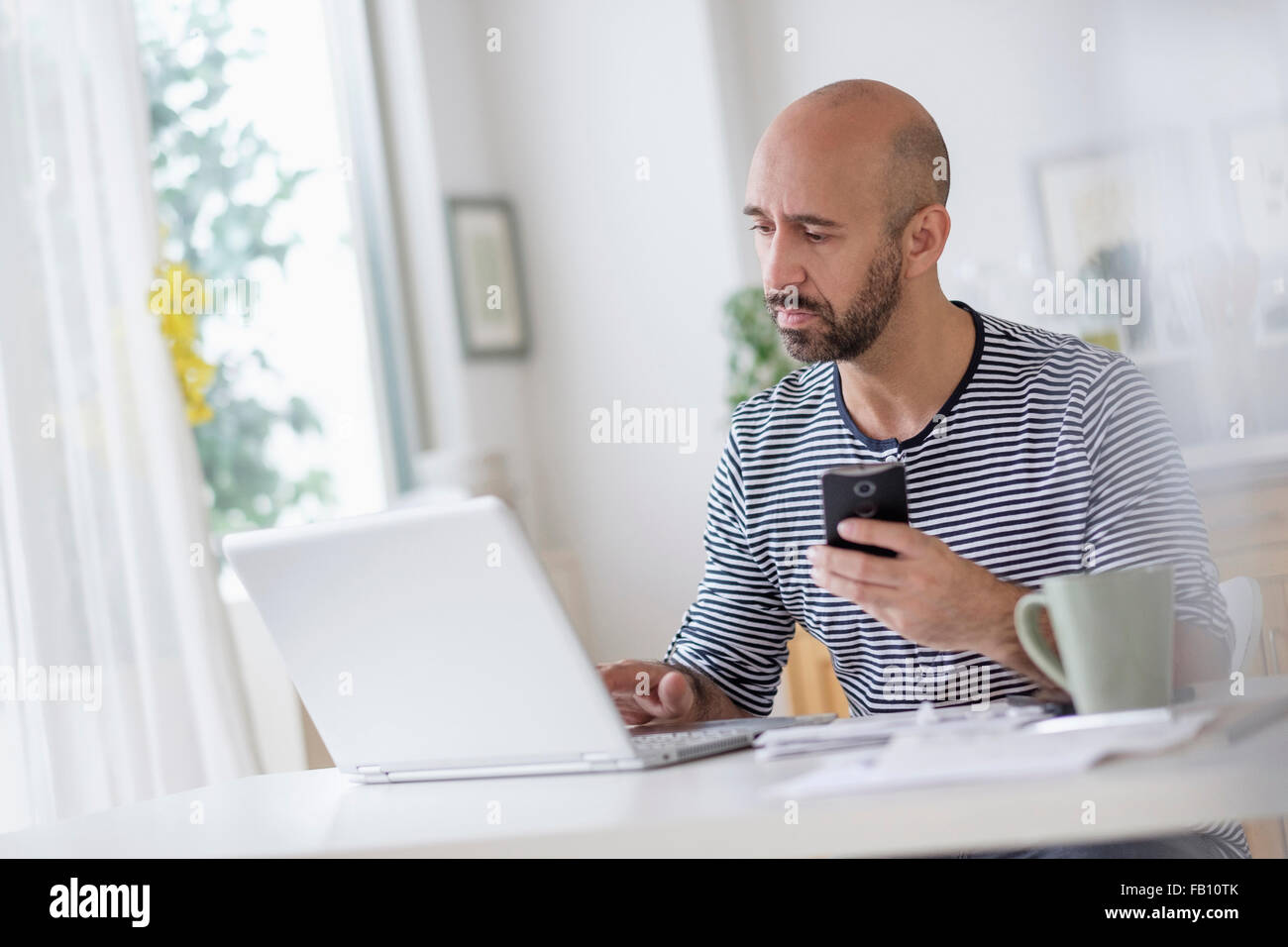 Mann mit Laptop und Smartphone am Tisch zu halten Stockfoto