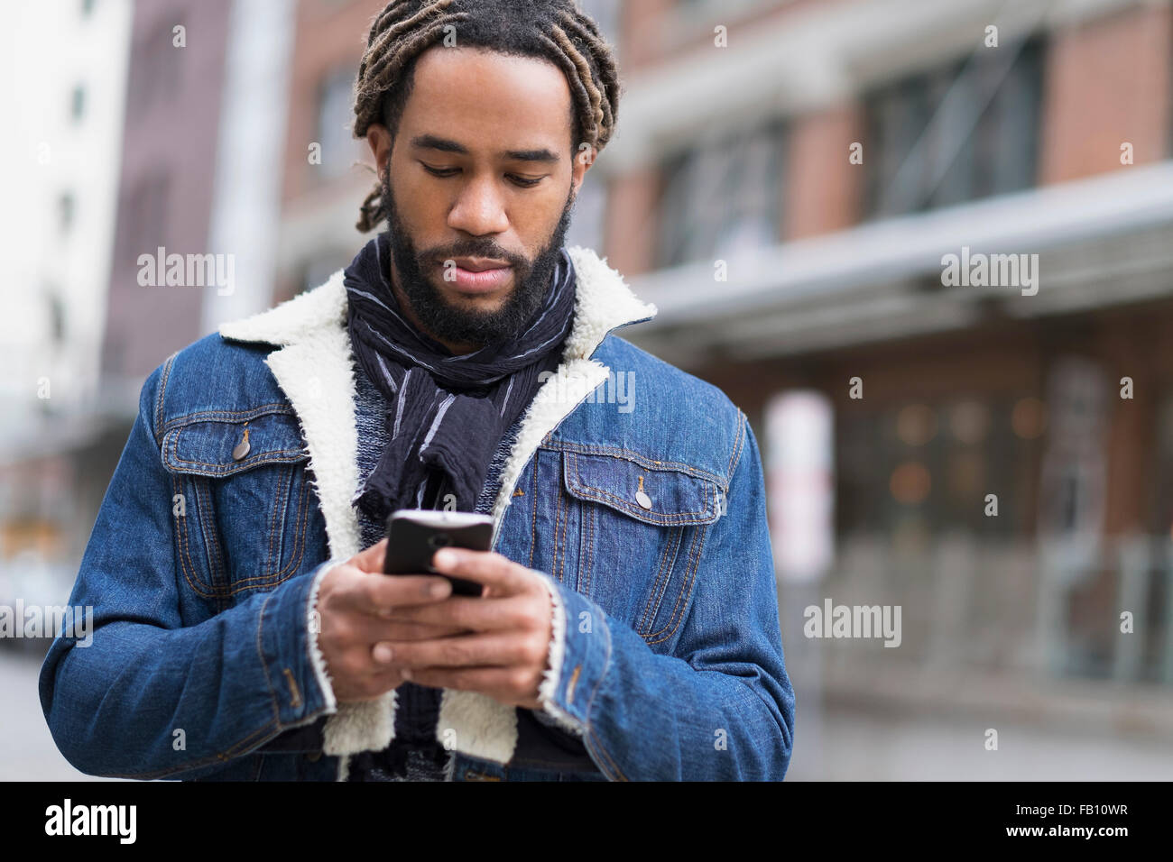 Ernster Mann mit Dreadlocks mit Smartphone in der Straße Stockfoto