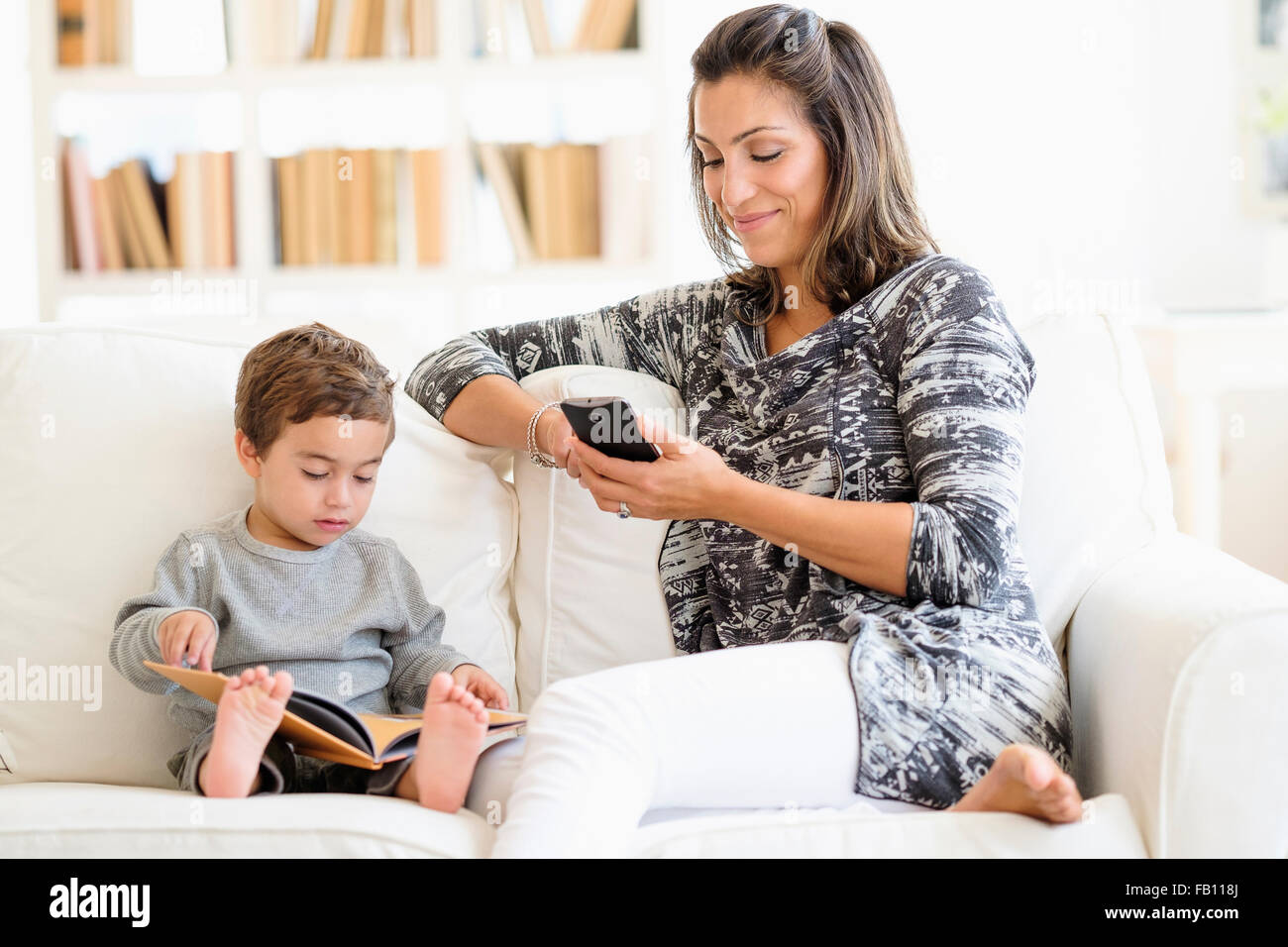 Mutter SMS während der Sohn (2-3) Lesung am sofa Stockfoto
