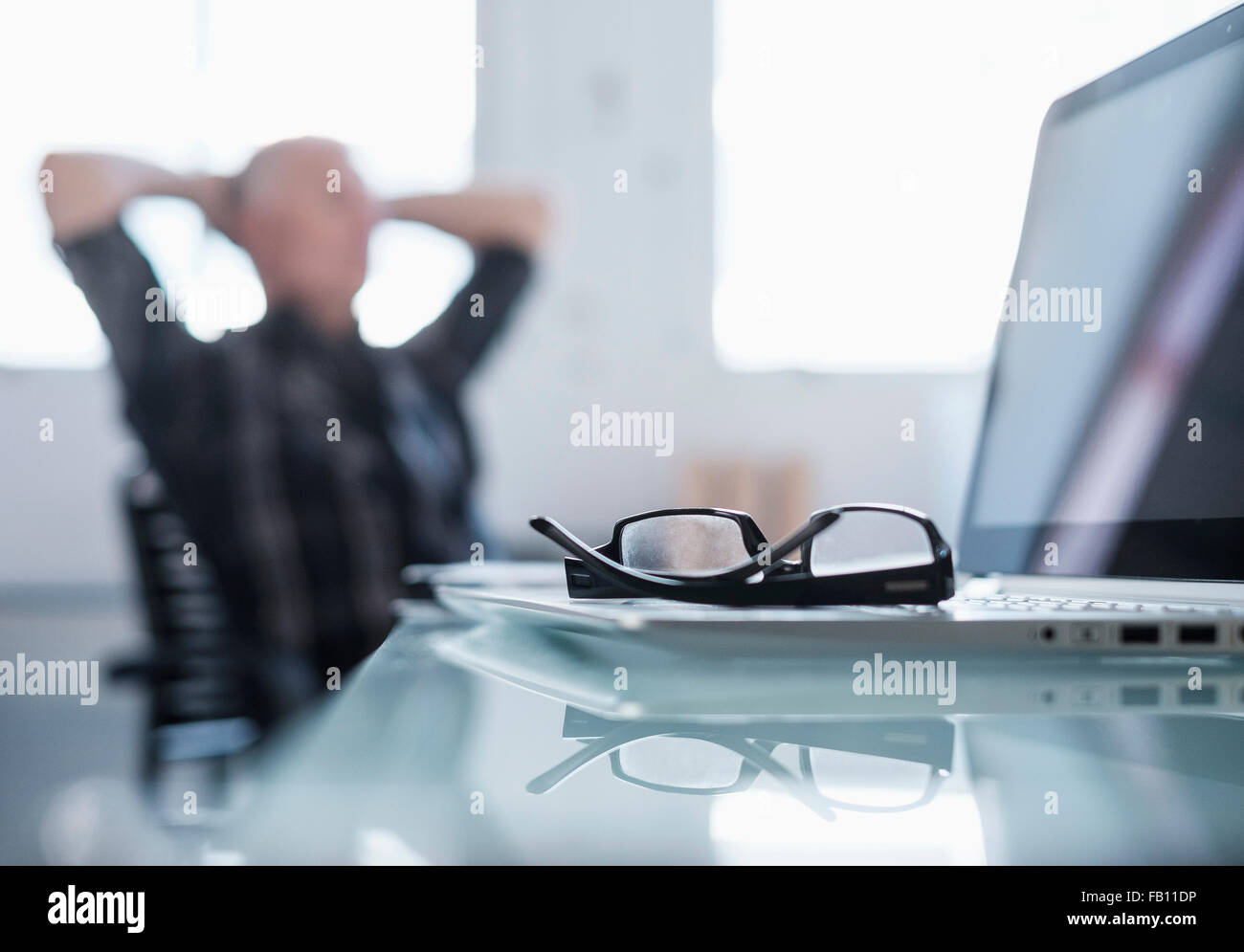 Brillen und Laptop am Schreibtisch im Büro, Mann im Hintergrund Stockfoto