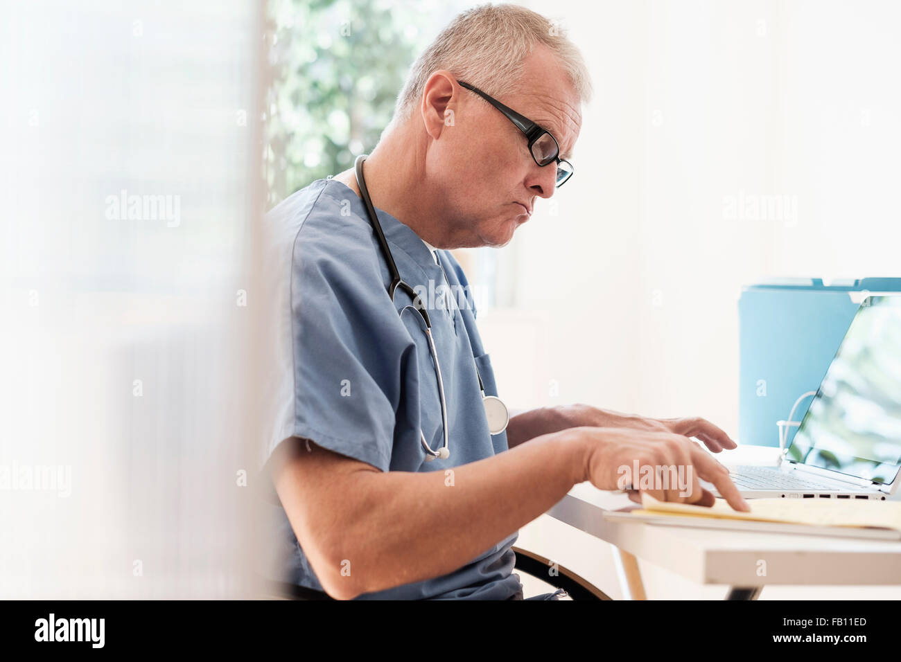 Mann in Scrubs mit Laptop in Arztpraxis Stockfoto