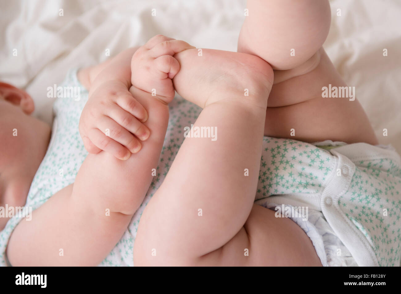 Babymädchen (12-17 Monate) liegend mit Händen auf Füßen Stockfoto