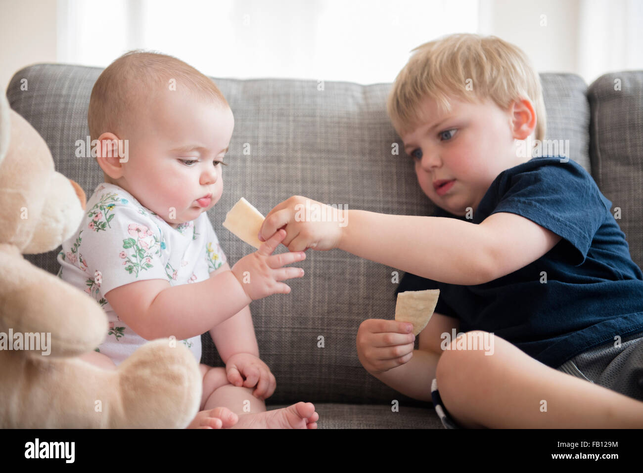 Bruder (2-3) Austausch von Cracker mit Babyschwester (12-17 Monate) Stockfoto