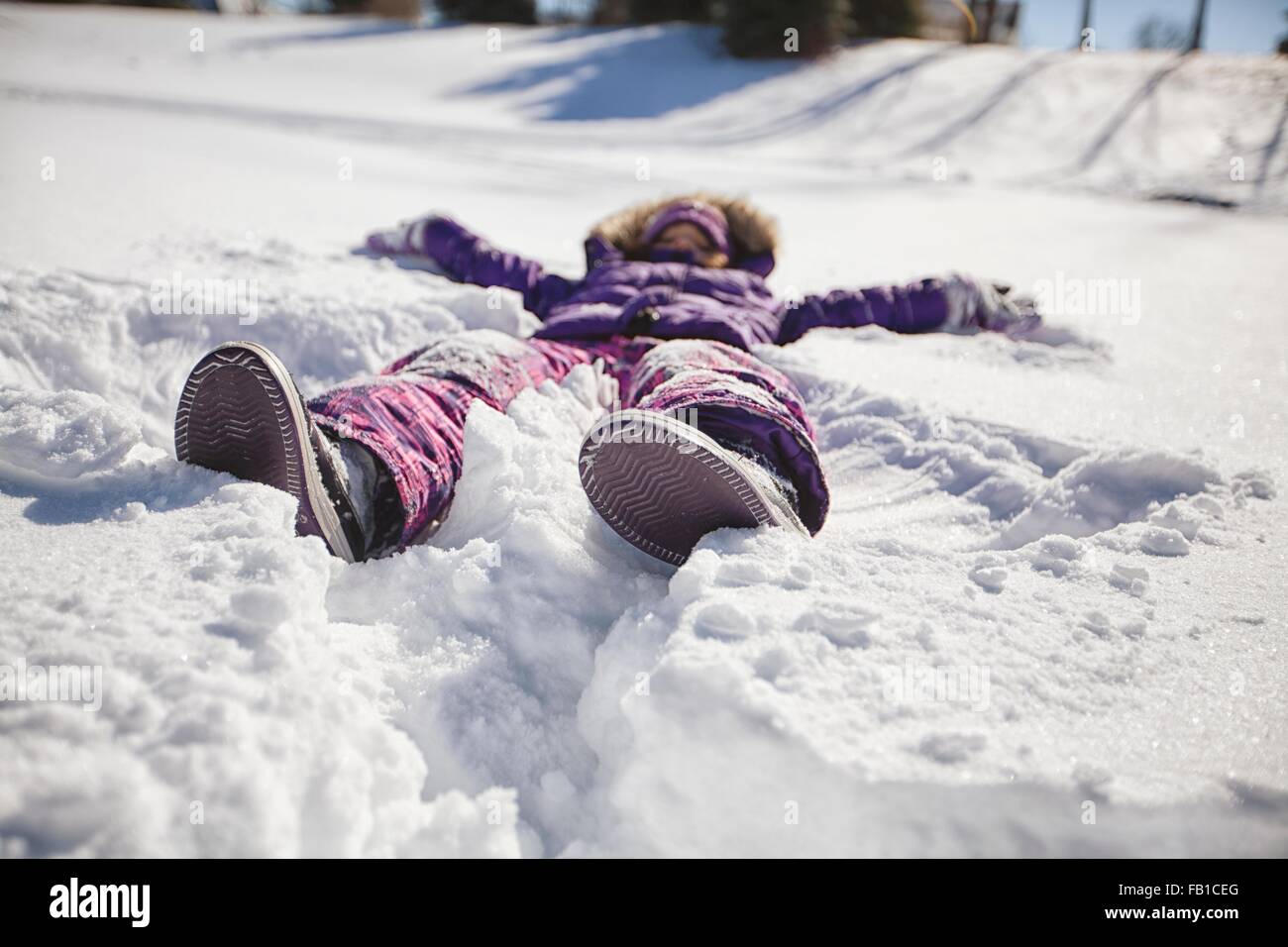 Ebene Oberflächenansicht von Mädchen trägt Ski Anzug liegender Schnee machen Schnee-Engel Stockfoto