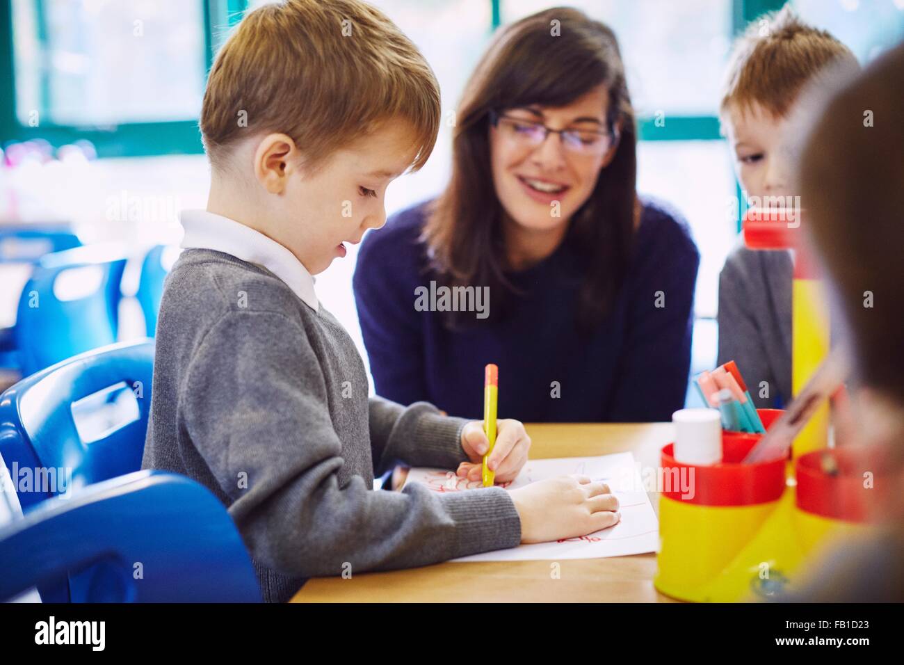 Jungen und Mädchen mit Lehrer zeichnen am Schreibtisch in der Grundschule Stockfoto