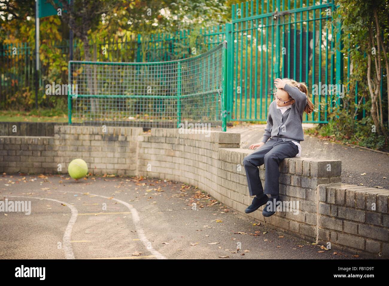 Elementare Schulmädchen auf Spielplatz Mauer sitzend Stockfoto