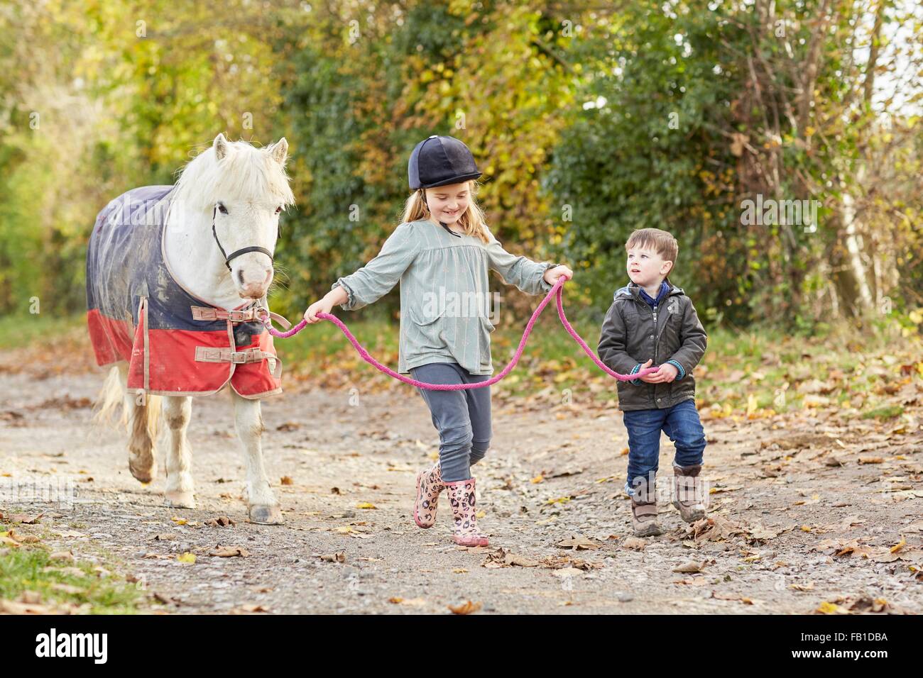 Junge und Schwester leading Pony entlang Landstraße Stockfoto