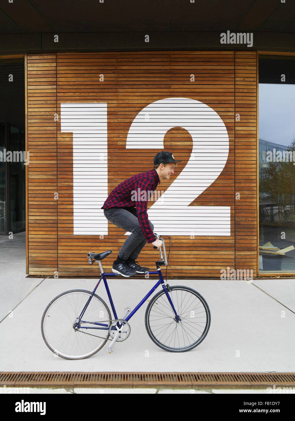 Urbane Radfahrer balancieren auf Fahrrad vor nummerierten Holzwand Stockfoto
