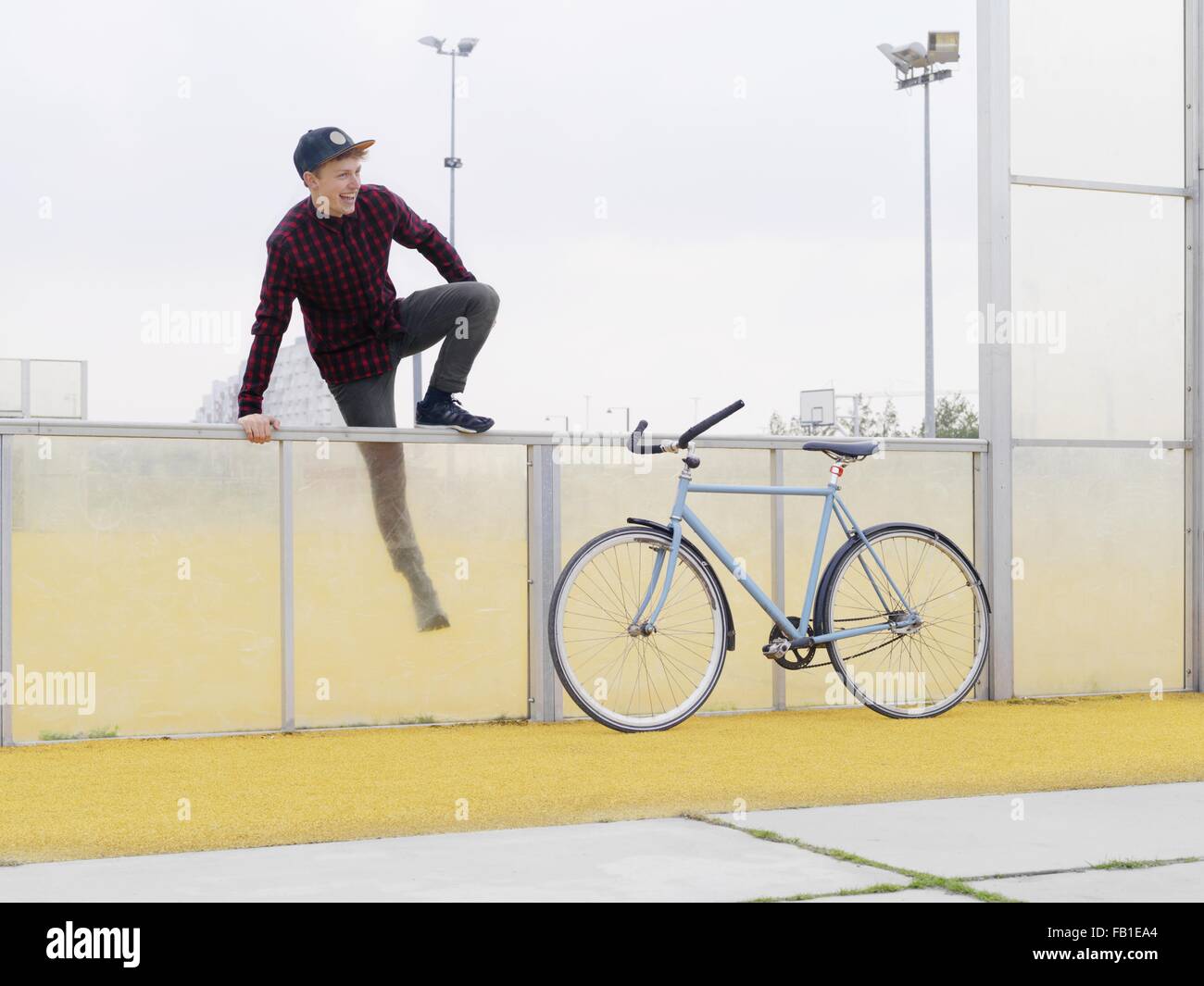 Urbane Radfahrer Klettern über den Zaun auf Sportplatz Stockfoto