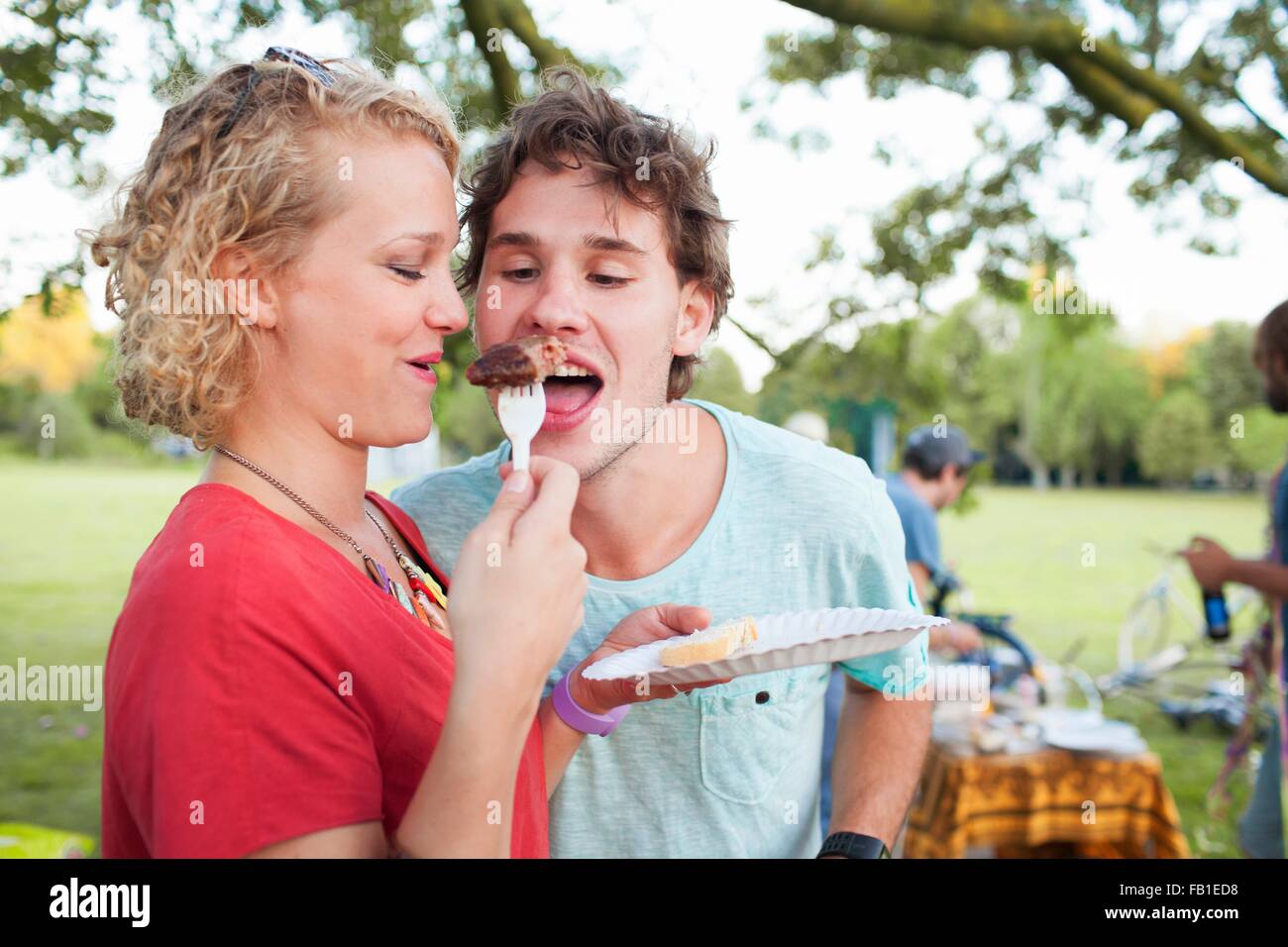 Glücklicher junger Mann und Frau teilen Essen bei Sonnenuntergang-Party im park Stockfoto