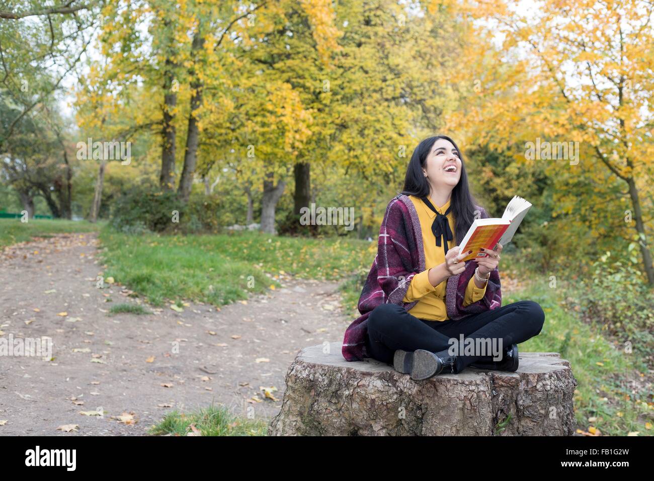 Junge Frau mit Buch auf Baumstumpf, Hampstead Heath, London Stockfoto