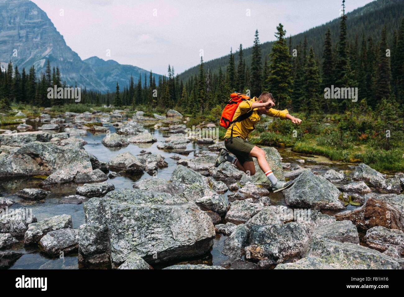 Seitenansicht der Mitte erwachsener Mann mit Rucksack springen über felsigen Flussbett, Moraine Lake, Banff Nationalpark, Alberta Kanada Stockfoto